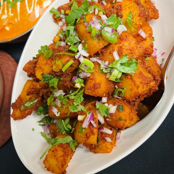 Spicy Indian potato dish, garnished with fresh cilantro, red onions, and green onions.