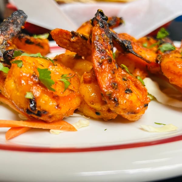 Close-up of vibrant orange Tandoori Shrimp garnished with fresh cilantro and shredded carrots.