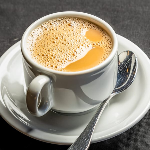Close-up of a white cup of frothy Indian chai tea on a saucer with a spoon.