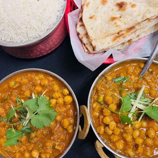 Two bowls of chickpea curry with cilantro and ginger, alongside rice and naan bread.
