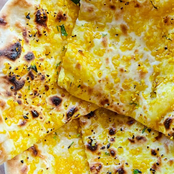 Close-up of golden Indian naan bread, topped with yellow lentils and herbs, from India Express Denver.
