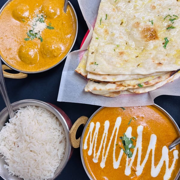 Three Indian dishes: malai kofta, butter chicken, and basmati rice, with a stack of naan bread.