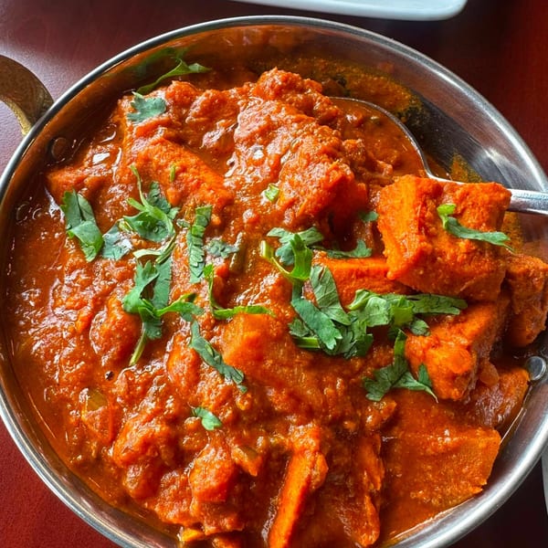 Close-up of a vibrant orange Indian curry with paneer cheese, garnished with fresh cilantro in a metal bowl.