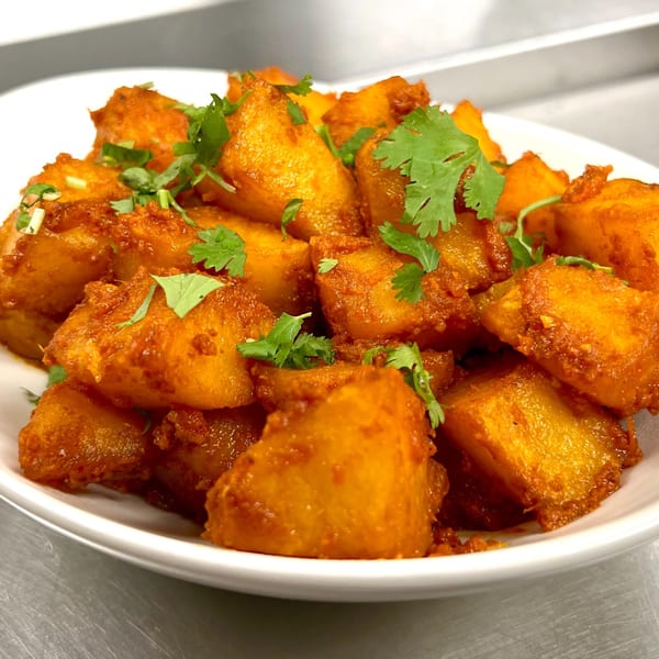 A white bowl filled with golden-brown Indian Express Denver aloo gobi, garnished with fresh cilantro.
