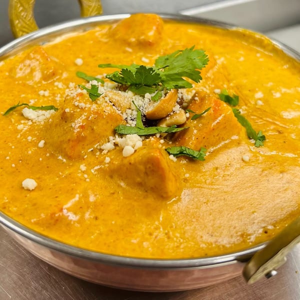 A copper bowl filled with creamy orange Indian butter chicken, garnished with cilantro and nuts.