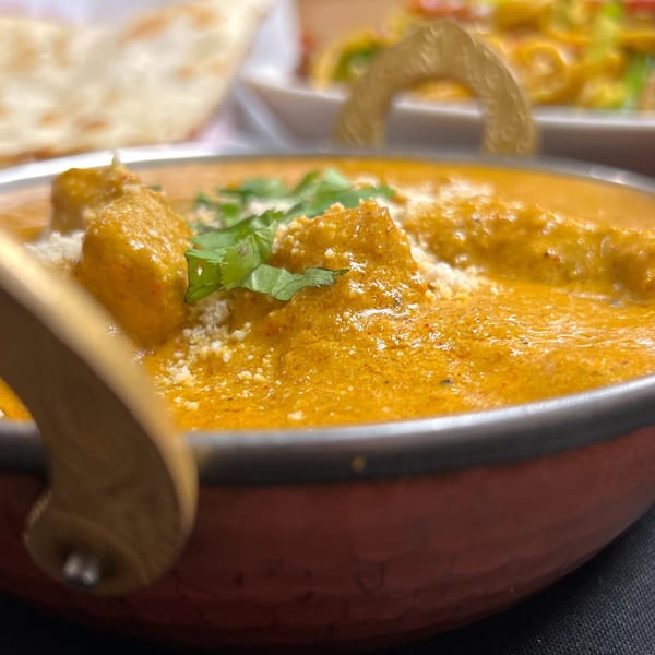Close-up of creamy orange Indian curry with paneer, cilantro, and grated cheese in a copper karahi.