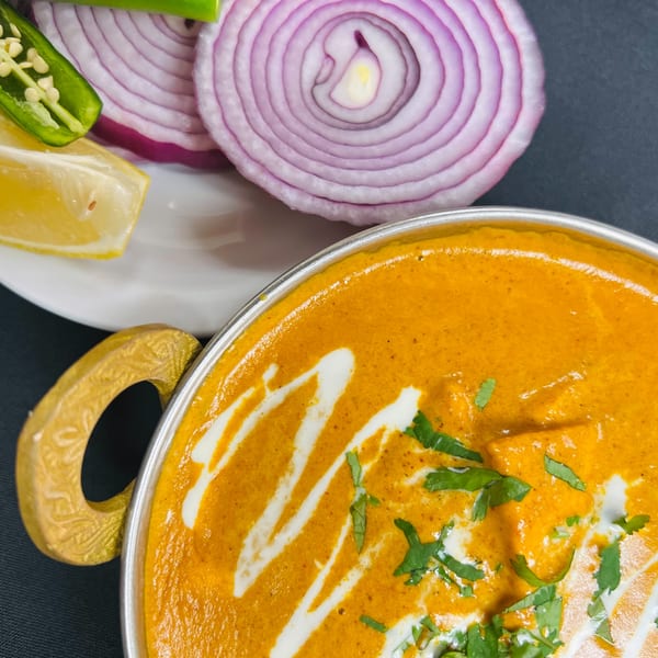 Indian Express Denver's butter chicken with cream swirls, cilantro, and a side of red onion, lemon, and jalapeño.