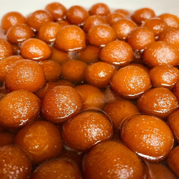 Close-up of many golden-brown Gulab Jamun, Indian fried dough balls, soaking in a sweet syrup.