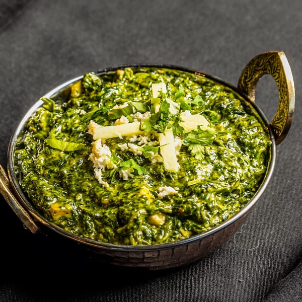 Palak Paneer, a vibrant green Indian spinach and cheese dish, in a decorative metal bowl.