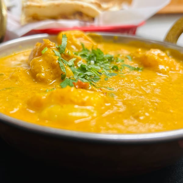 Close-up of a bowl of vibrant orange Indian curry, garnished with fresh green cilantro.