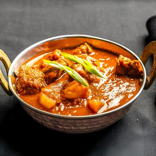Indian Express Denver's lamb curry with potatoes and green onions in a metal bowl.