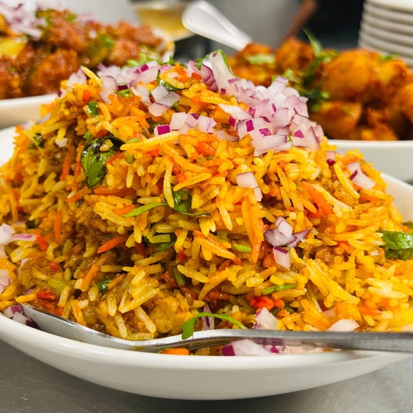 A close-up of vibrant Indian biryani with rice, vegetables, and red onions in a white bowl.