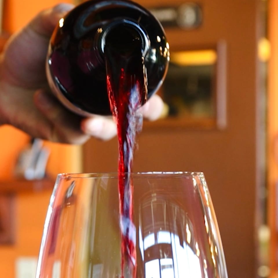 Red wine pouring from a bottle into a clear glass, with a warm, inviting background.