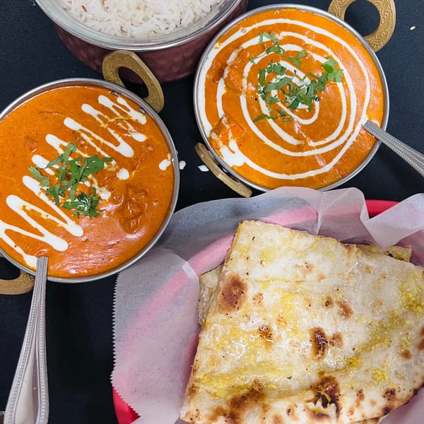 Two bowls of Indian curry with cream swirls and cilantro, rice, and naan bread.