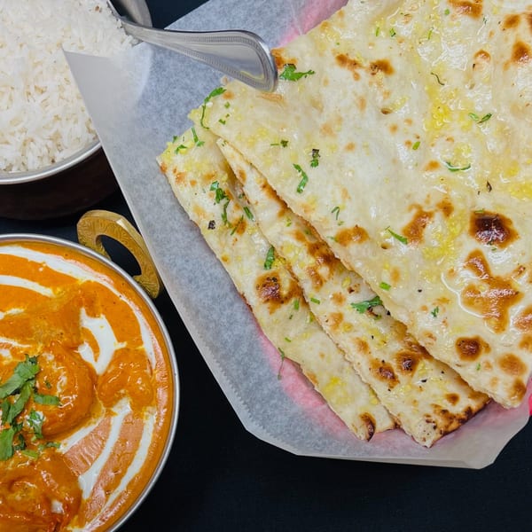 Indian butter chicken, white rice, and garlic naan bread with cilantro on a black surface.
