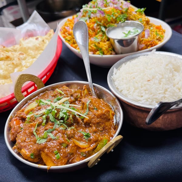A spread of Indian dishes, including chicken curry, biryani, white rice, and naan bread.