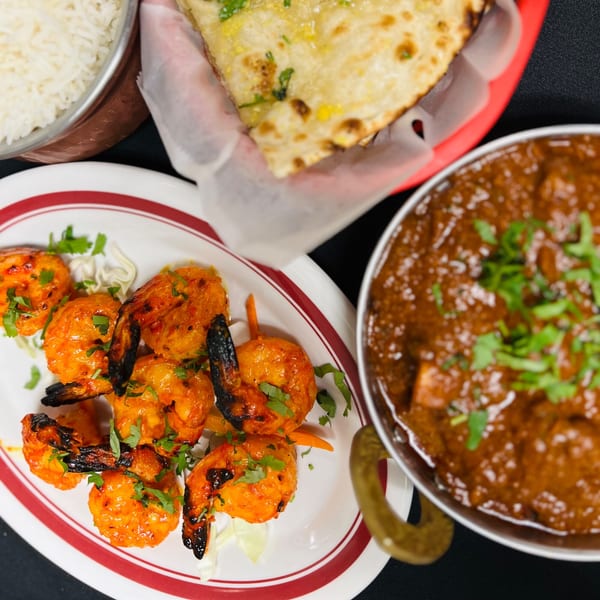 Indian Express Denver's grilled shrimp, naan, rice, and curry dish on a dark surface.