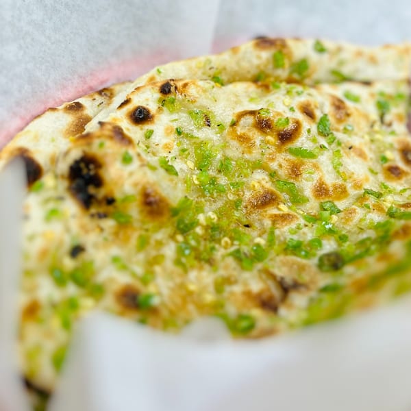 Close-up of garlic naan from India Express Denver, topped with green herbs and sesame seeds.