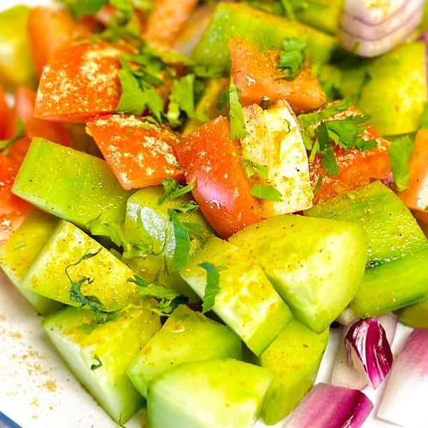 Close-up of a fresh Indian salad with diced tomatoes, cucumbers, red onions, and cilantro.