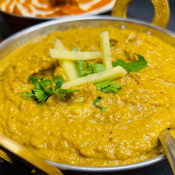 Close-up of a golden Indian curry, garnished with fresh cilantro and ginger matchsticks, in a metal bowl.