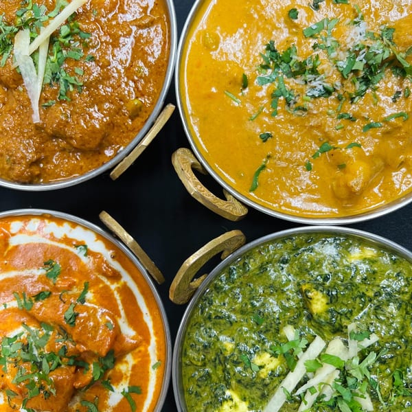 Four bowls of Indian curries, including butter chicken, palak paneer, and other vibrant dishes.