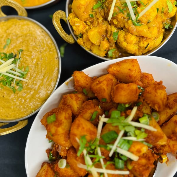 Three bowls of Indian food, including a creamy yellow curry, cauliflower and potato curry, and spiced potatoes.