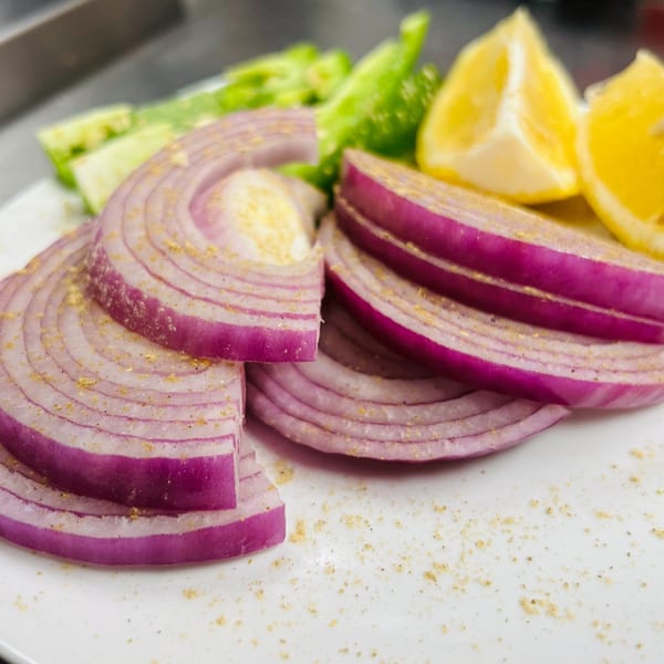 Sliced red onions seasoned with spices, green peppers, and lemon wedges on a white plate.