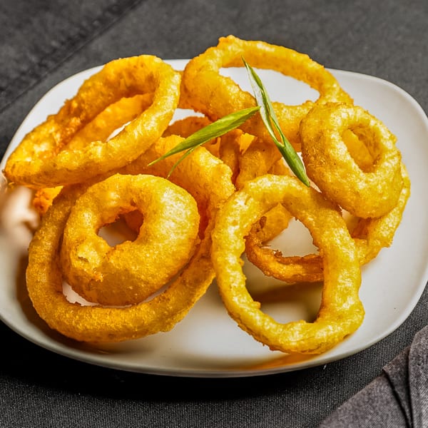 Golden-brown onion rings, garnished with green onions, on a white plate at India Express Denver.