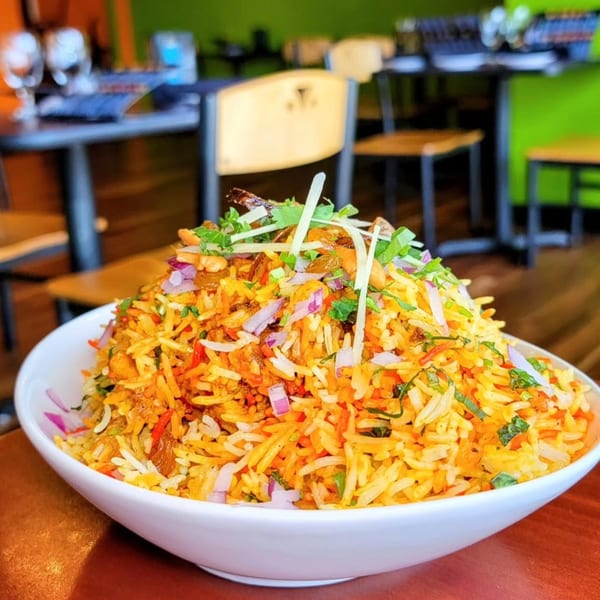 A large bowl of India Express's biryani, topped with onions, nuts, and herbs, in a restaurant setting.