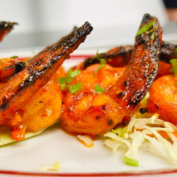 Close-up of vibrant orange Indian Express tandoori shrimp with charred tails, garnished with fresh cilantro.