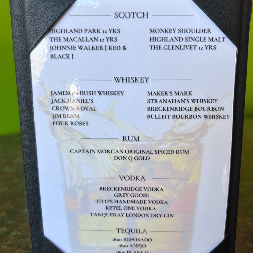 A close-up of a laminated drink menu featuring Scotch, Whiskey, Rum, Vodka, and Tequila selections.