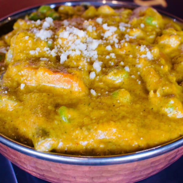 Close-up of a vibrant yellow Indian curry with vegetables and crumbled cheese in a copper bowl.