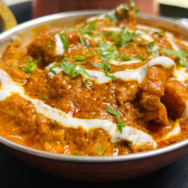 Close-up of creamy orange Indian curry with white swirls and fresh green herbs in a copper bowl.