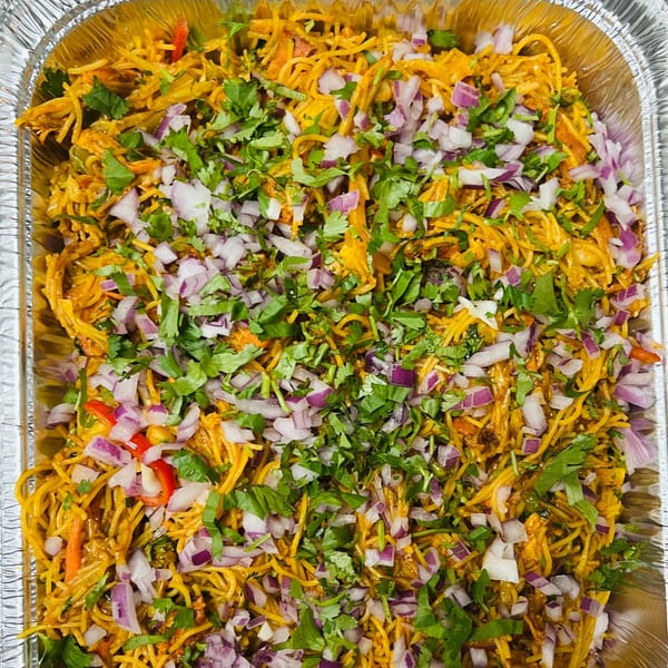 A large foil tray filled with Indian Express Denver's yellow noodles, topped with red onions and cilantro.