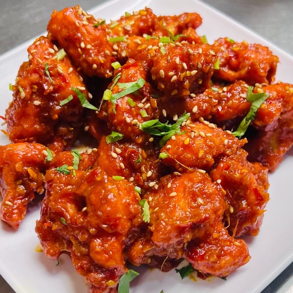 Close-up of India Express Denver's vibrant orange chili chicken, garnished with sesame seeds and green herbs.