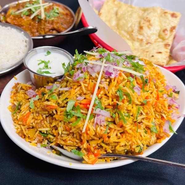 A vibrant Indian biryani dish with rice, vegetables, and spices, garnished with red onions and cilantro.