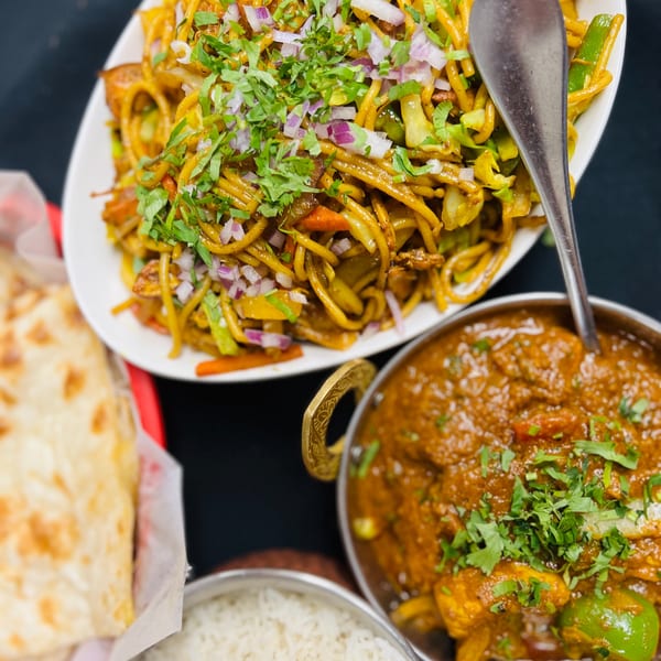 Indian Express Denver's chicken curry, noodles, rice, and naan bread on a dark surface.