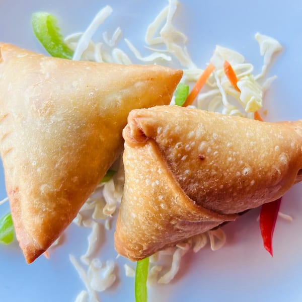 Two golden-brown Indian samosas on a white plate, garnished with shredded cabbage, carrots, and green peppers.