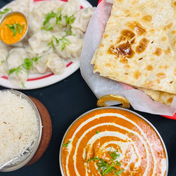 A top-down view of Indian food, including momos, naan, rice, and a creamy orange curry.