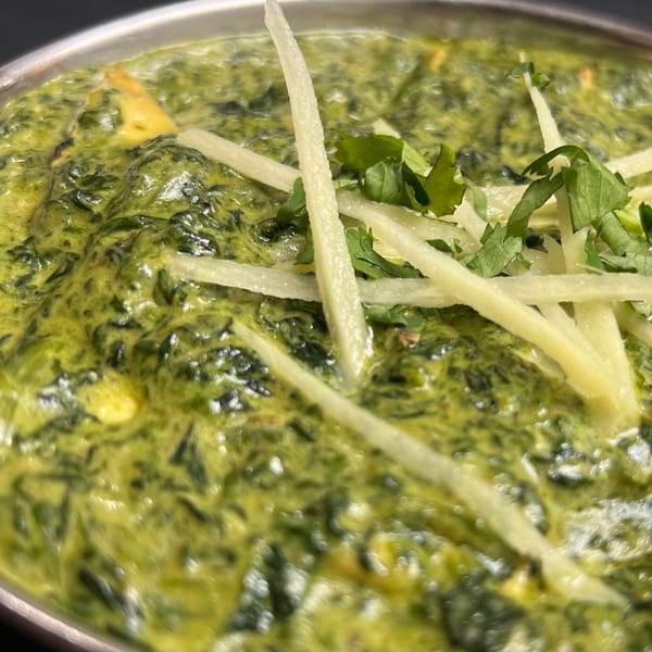 Close-up of vibrant green Palak Paneer, garnished with fresh cilantro and ginger juliennes.