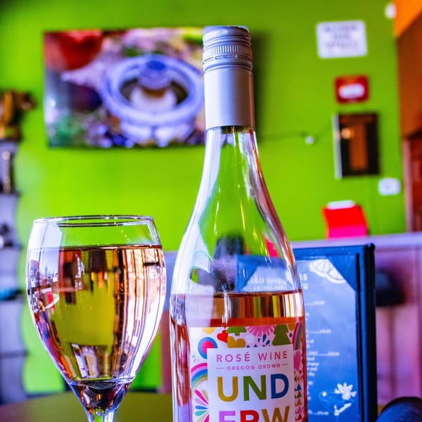 A bottle of rosé wine and a glass of wine on a table with a bright green background.