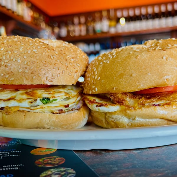 Two egg and tomato sandwiches on sesame seed buns, on a white plate at India Express Denver.