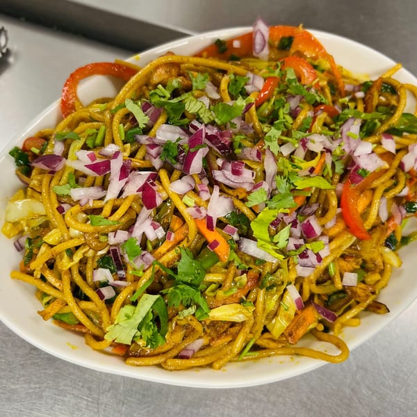 A close-up of Indian noodles with red onions, bell peppers, and cilantro in a white bowl.