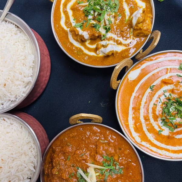 Three bowls of Indian curries with cream and cilantro, alongside two bowls of white rice.