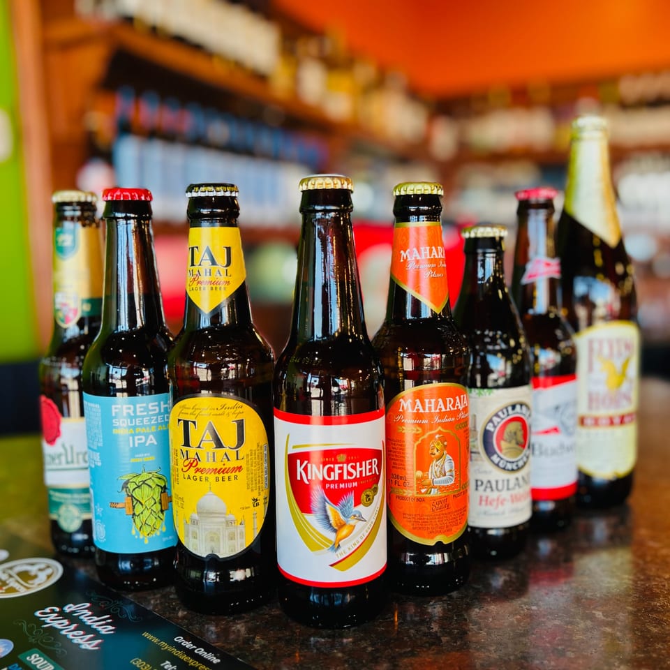 A variety of Indian and international beer bottles, including Taj Mahal and Kingfisher, on a bar.