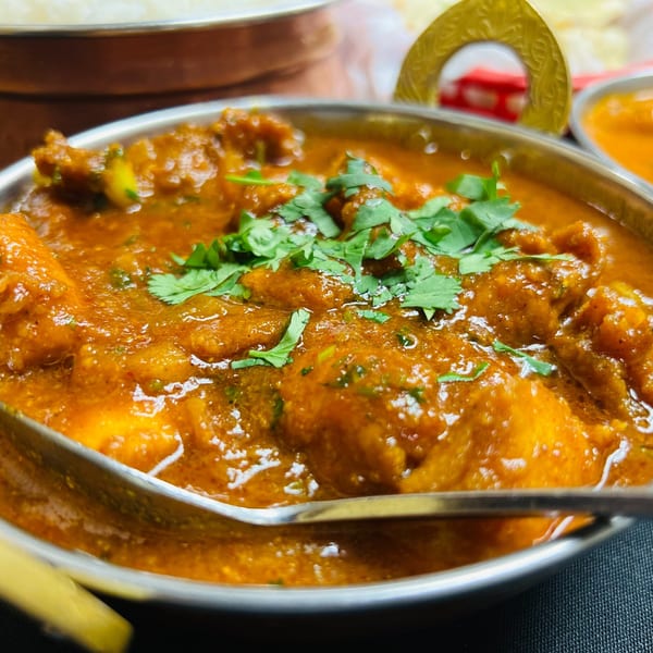 Close-up of India Express Denver's chicken curry, garnished with fresh cilantro in a metal bowl.