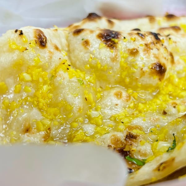 Close-up of golden-brown garlic naan bread, glistening with butter and minced garlic.