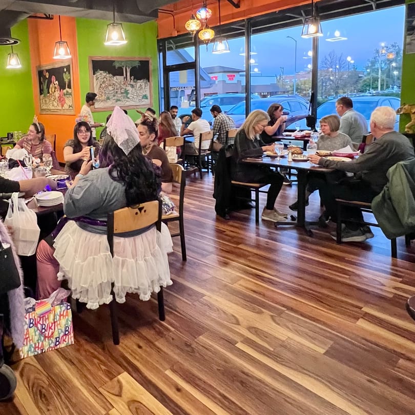 Diners enjoy a birthday celebration in a vibrant restaurant with large windows.