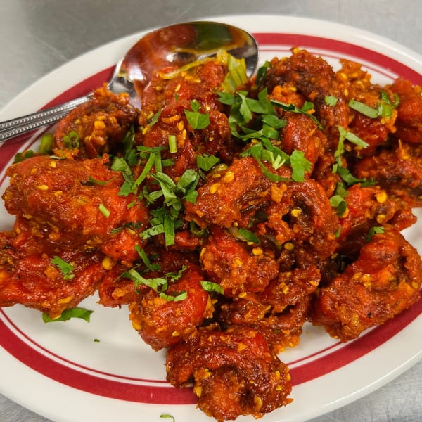 Close-up of India Express Denver's vibrant red Indian chili chicken, garnished with fresh green herbs.