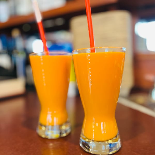 Two glasses of bright orange mango lassi with red straws on a brown table at India Express Denver.